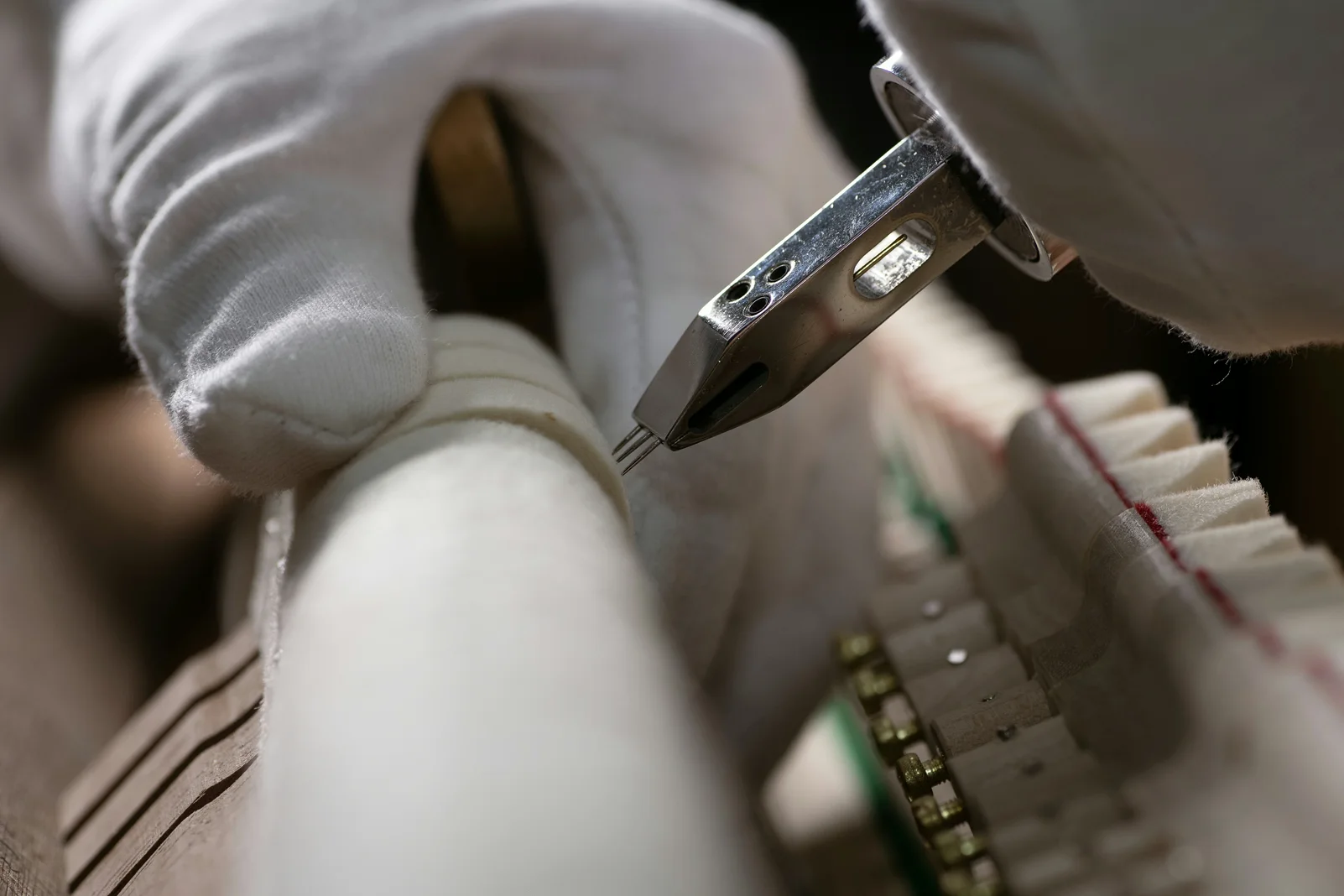 A technician wearing white gloves needles the hammer felt during voicing