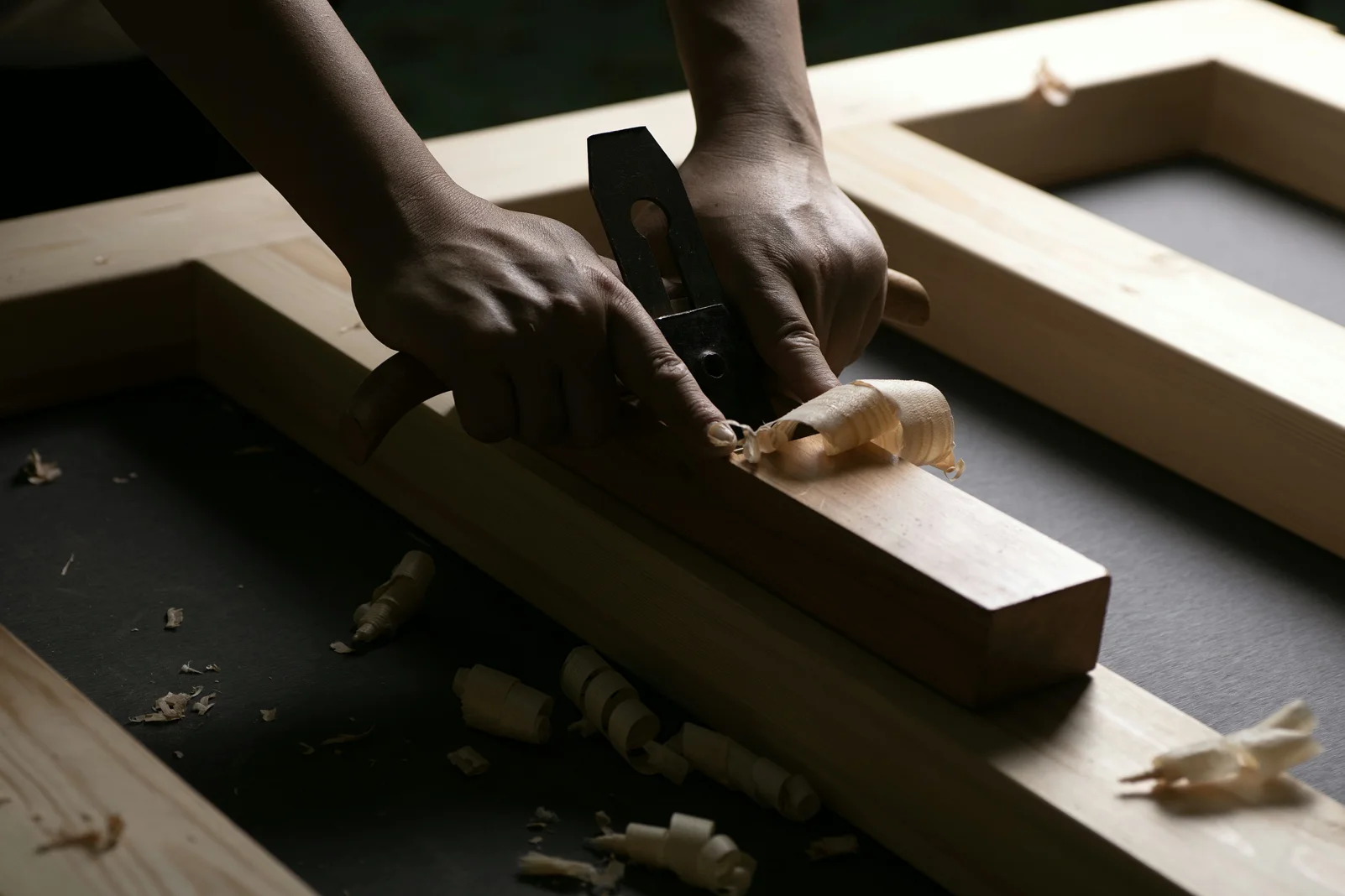 Hands guiding a wood plane as a shaving curls from the timber