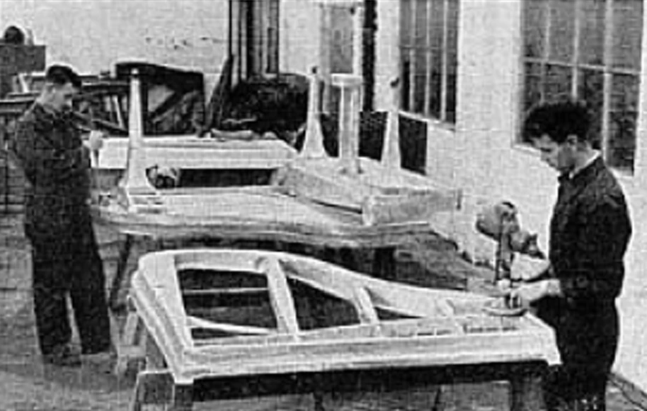 Black-and-white archive photograph of workers beside rows of piano frames